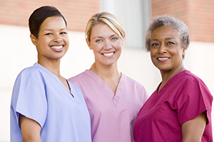Three nurses in different color scrubs all smiling at the camera