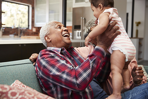 A smiling grandfather holding his infant granddaughter up in the air to amuse her