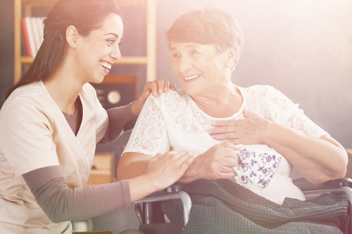 Young nurse knelt down next to smiling elderly woman in a wheelchair