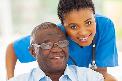 Young nursing in blue scrubs leaning over the shoulder of patient in wheelchair smiling 