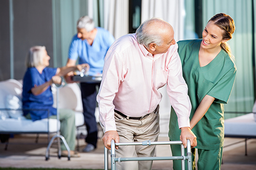 Focus on nurse assisting man with walker, background out of focus of Dr assisting another patient